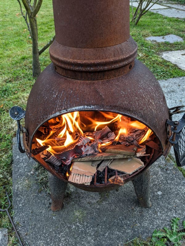 a rusty metal fire pit with a fire burning